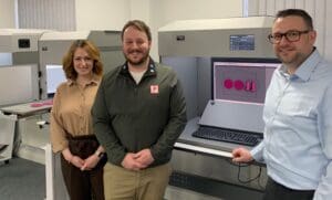 Adam from Verivide and Jess and Will from plastikcity standing beside a workstation displaying